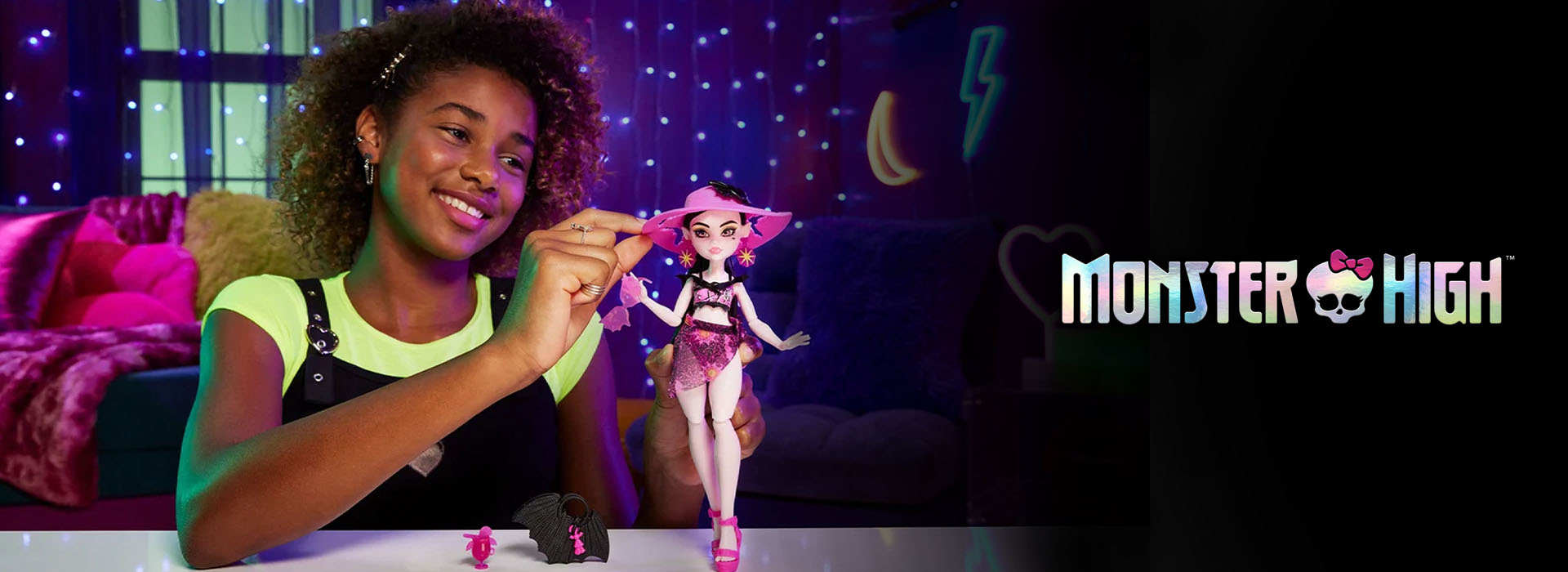 Mädchen spielt mit Puppe in lichtdekoriertem Raum, Monster High-Logo sichtbar.
