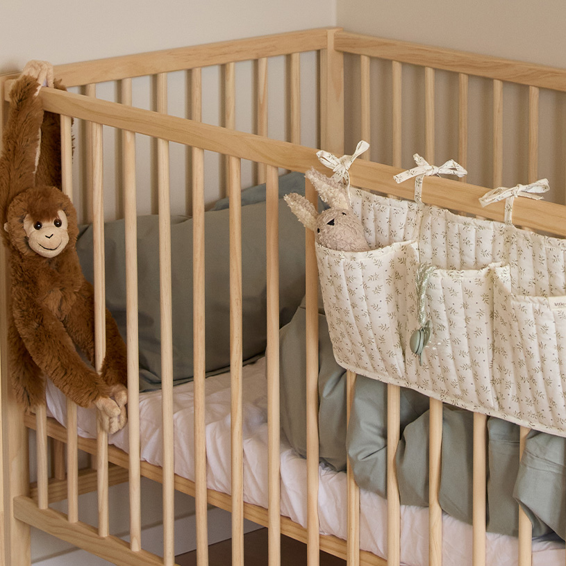 Weißes Kinderbett mit Mobile und Kuscheltieren.
