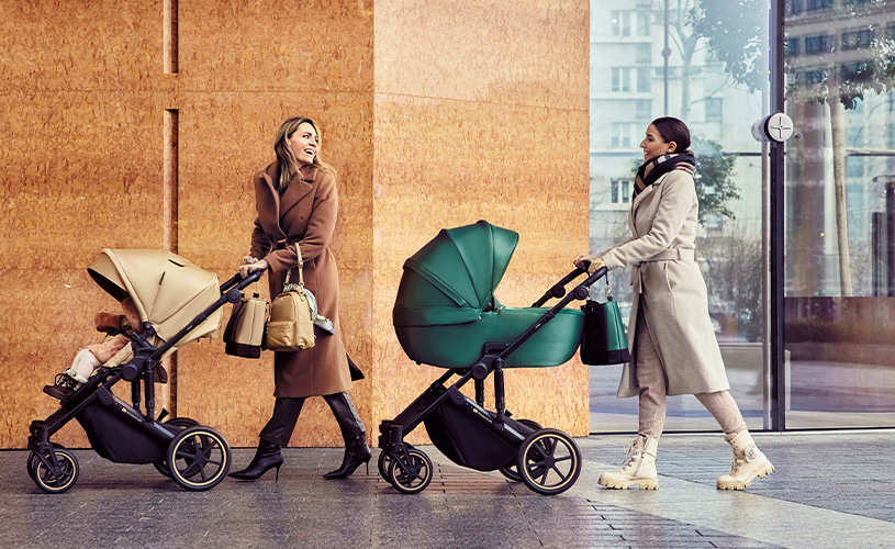 Zwei Frauen gehen draußen und sprechen, mit beigem und grünem Kinderwagen.