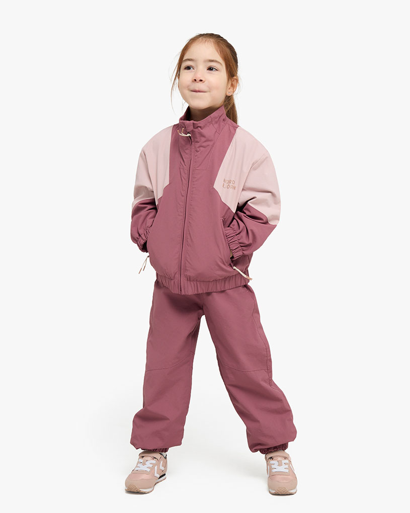 Mädchen in rosa gestreifter Kleidung und Mütze spielt draußen.
