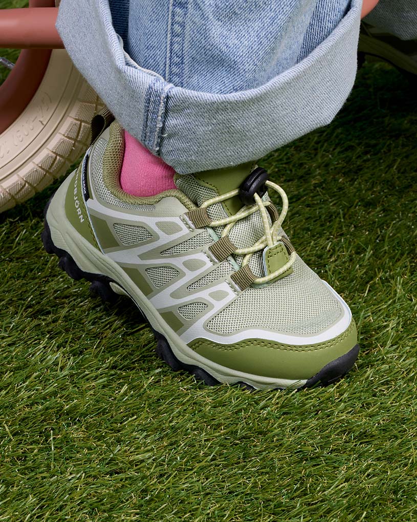 Grüne Kinderschuhe mit Klettverschluss und weißen Akzenten an Füßen in weißen Socken.