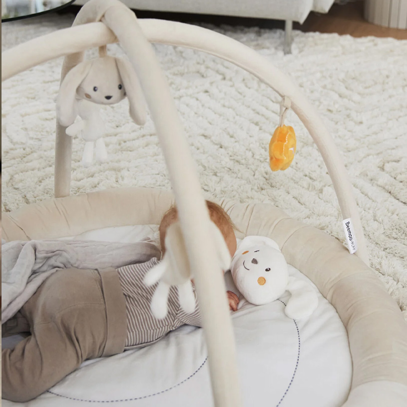Ein Baby liegt auf einer Spielmatte mit hängendem Spielzeug darüber.