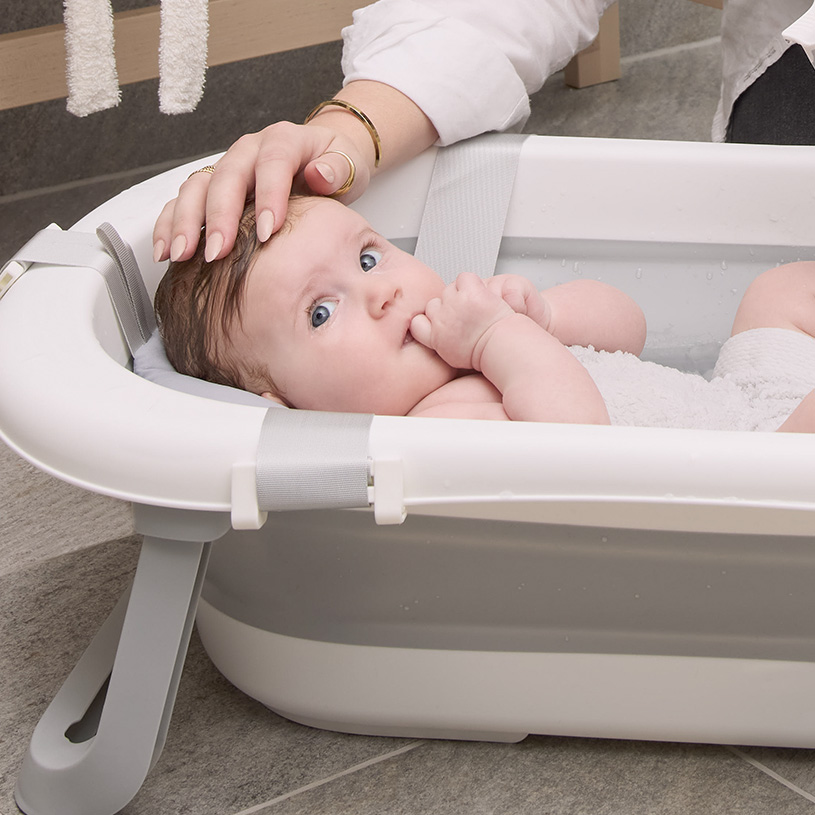 Baby in einer Badewanne mit Hand am Kopf.