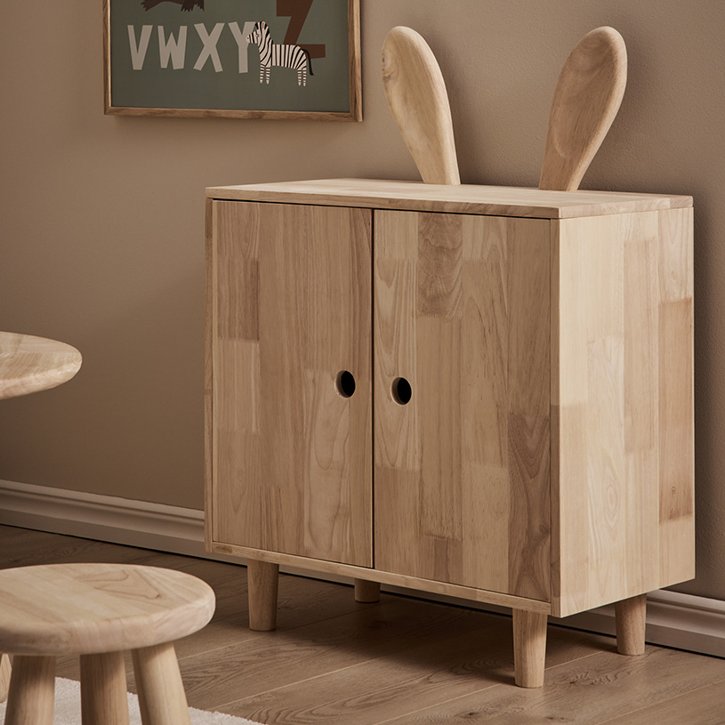 Holzschrank mit Kaninchenohren oben, vor einer beigen Wand.
