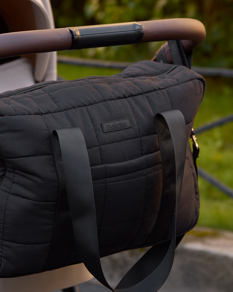 Schwarze gesteppte Wickeltasche am Kinderwagengriff draußen.
