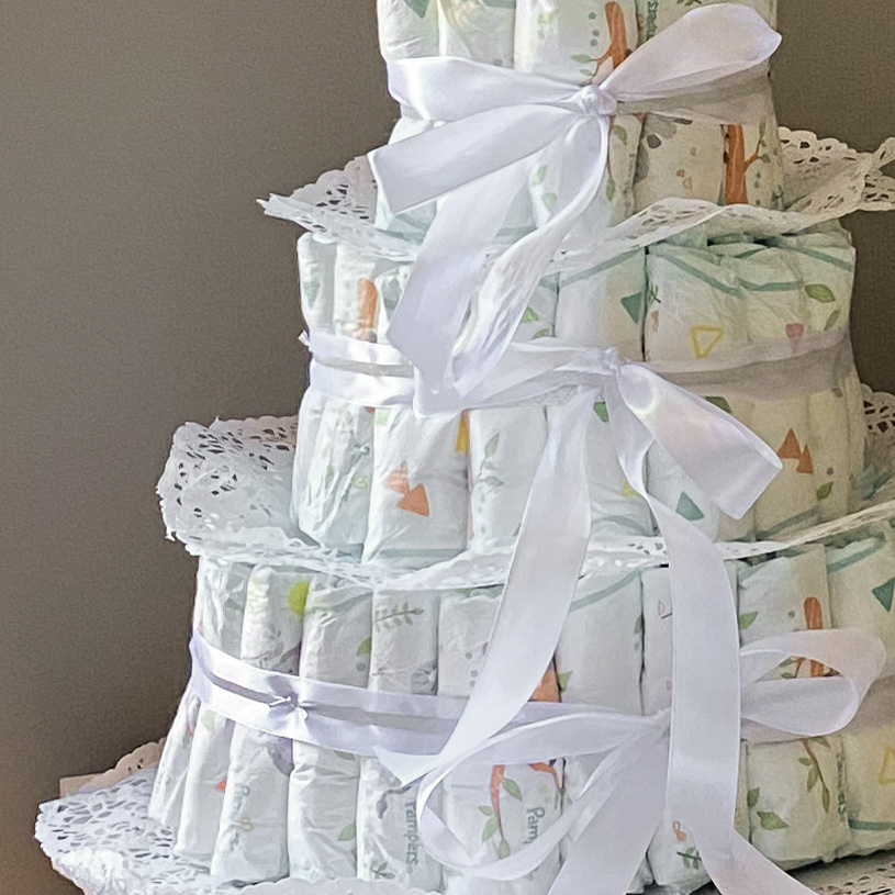 Windeltorte mit drei Ebenen, dekoriert mit weißen Bändern und einem Kuschelhasen oben.