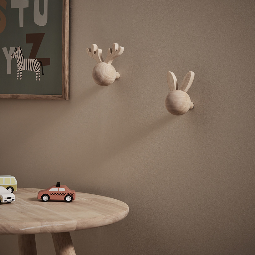 Wandhaken aus Holz mit Hörnern und Ohren neben Spielzeugautos auf einem Tisch.