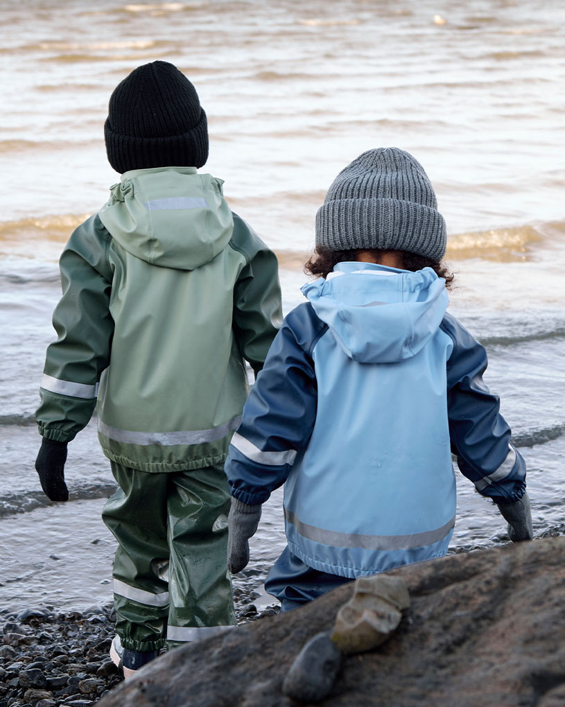 Zwei Kinder in Regenkleidung spielen am Wasserstrand.