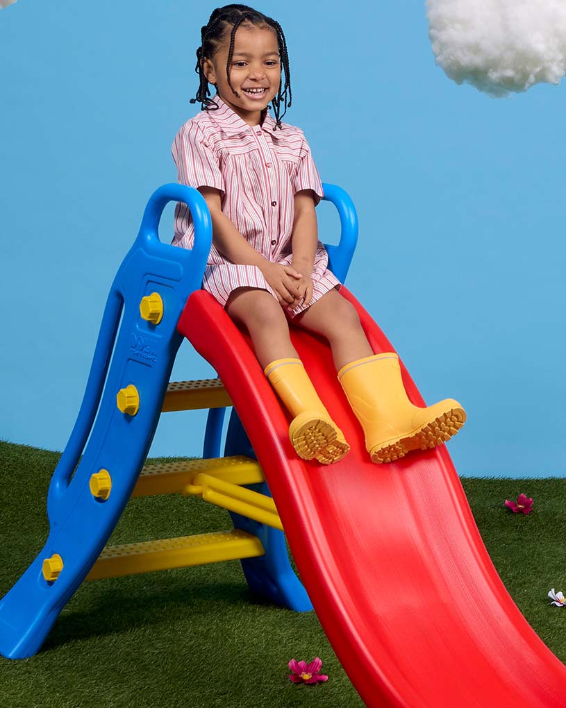 Kind mit rosa Hut rutscht auf einer Rutsche.