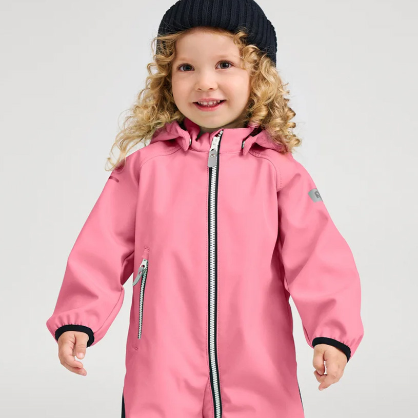 Lächelndes Kind in orangefarbener Jacke und lila Mütze.