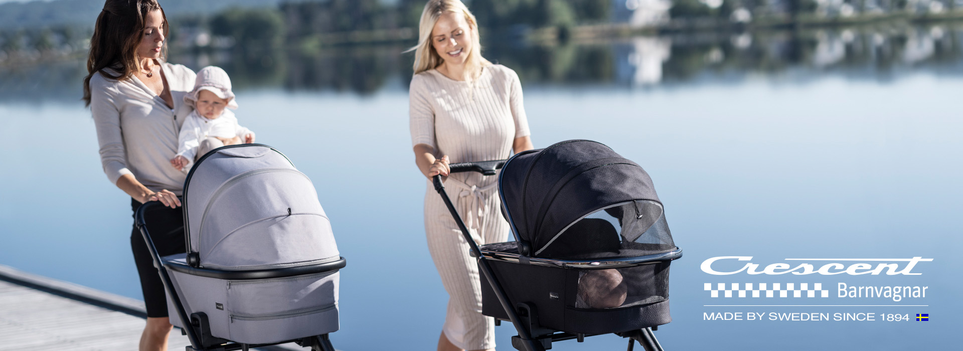 Zwei Frauen gehen mit Kinderwagen am See spazieren.