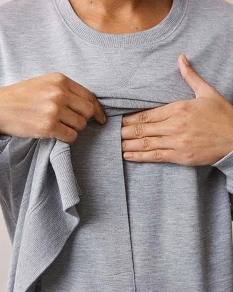 Person zeigt Tasche auf grauem Pullover.