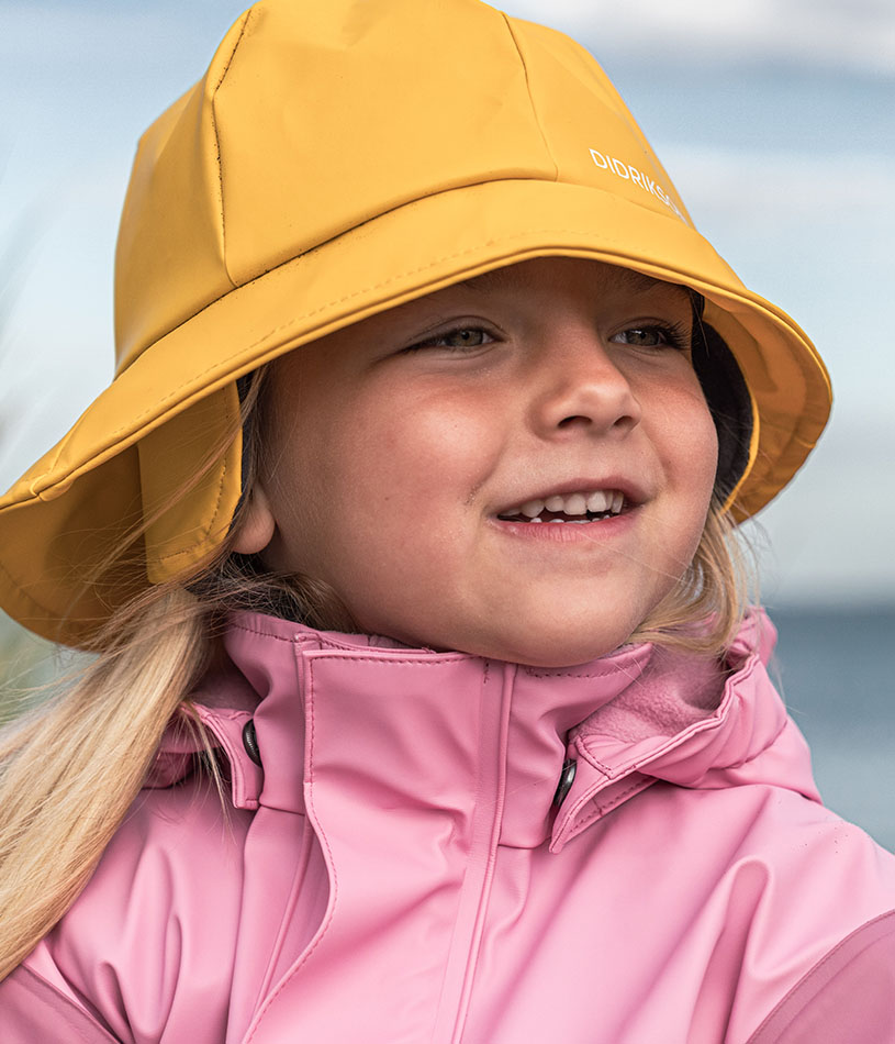 Kind in rosa Regenjacke und Hut lächelt im Freien.