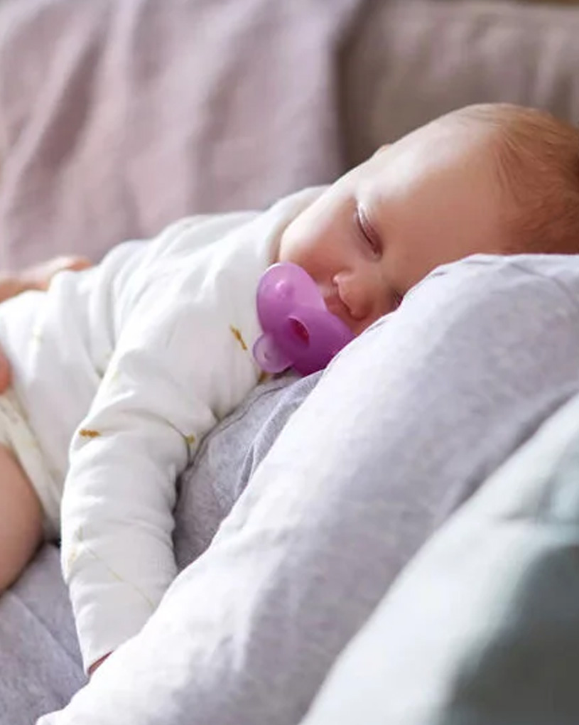 Baby schläft mit Schnuller im Mund auf einem Erwachsenen.