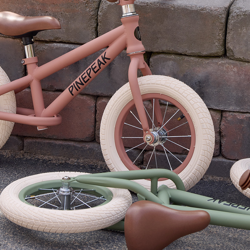 Gelbes Kinderfahrrad mit Korb und Stützrädern vor Kissen und Wand.