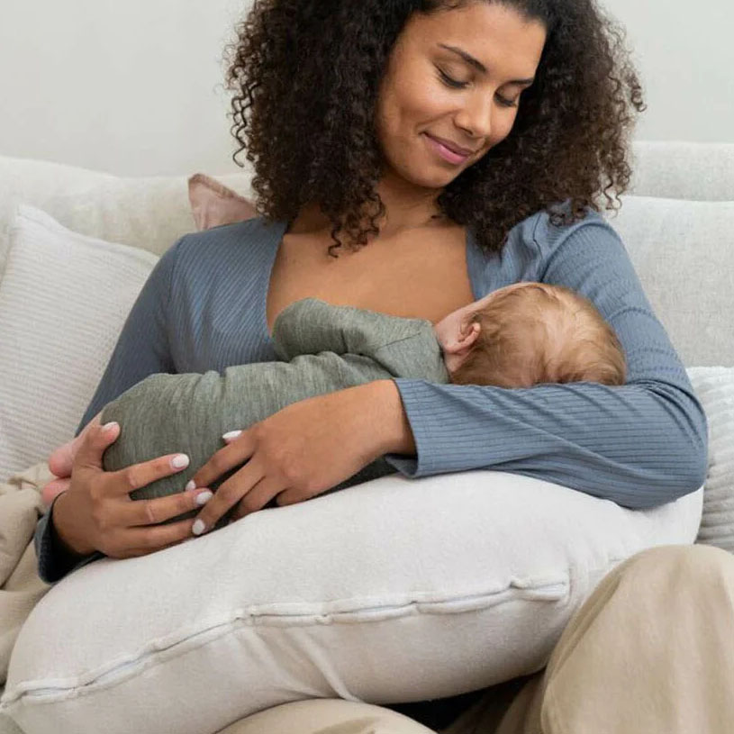 Eine Frau stillt ein Baby, das auf einem Kissen im Sofa liegt.