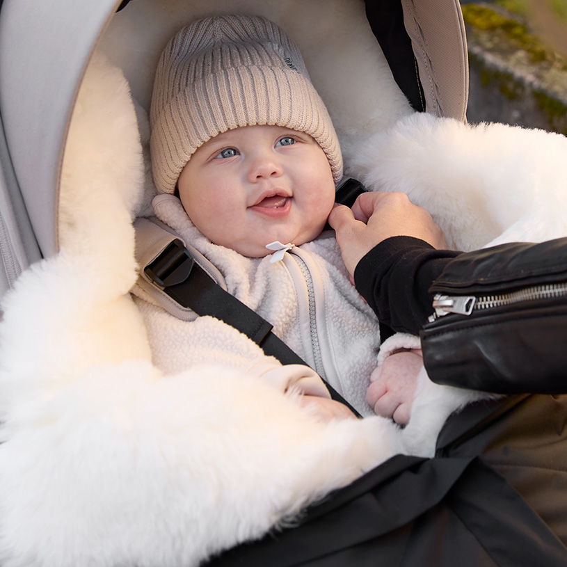 Baby mit Schnuller schläft in schwarzem Anzug im Autositz.
