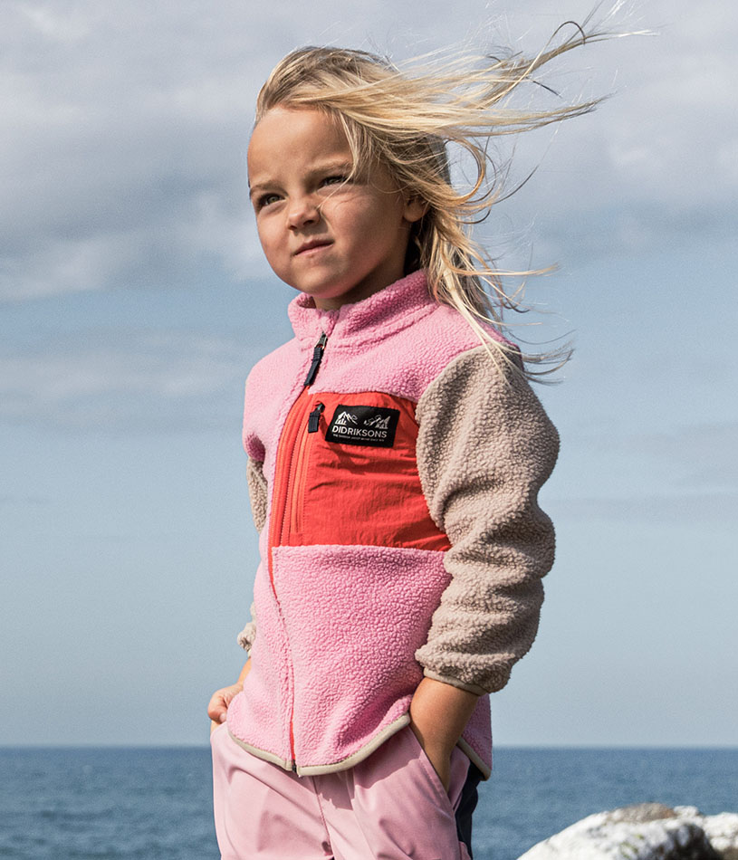 Ein Kind in bunter Fleecejacke steht an einem See.