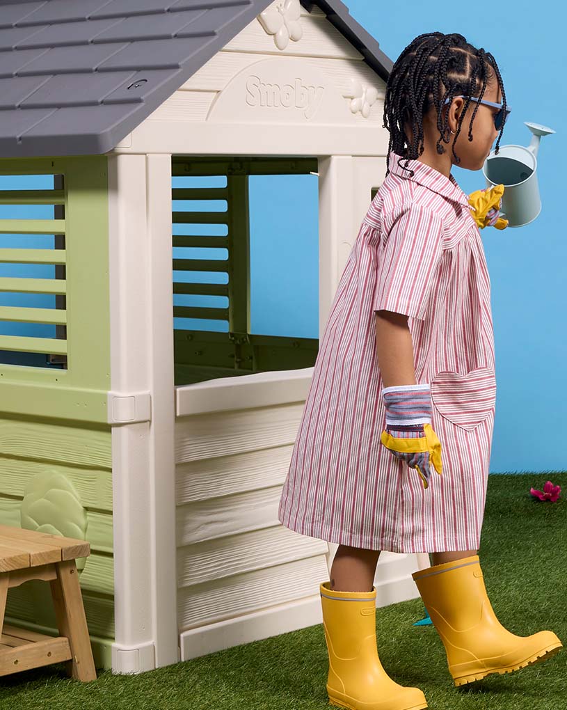 Kind in grüner Jacke schaut durch Fenster eines weißen Gebäudes.