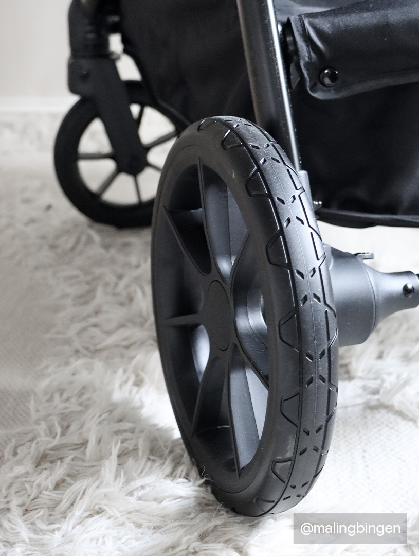 Nahaufnahme schwarzer Kinderwagenräder auf einem weißen Teppich.