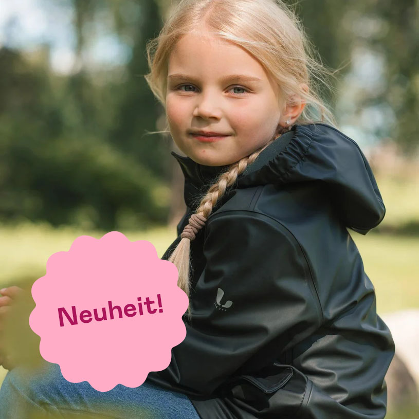 Kind im Hundemuster-Anzug im Garten, rosa Schild mit 'Neuheit!' drauf.