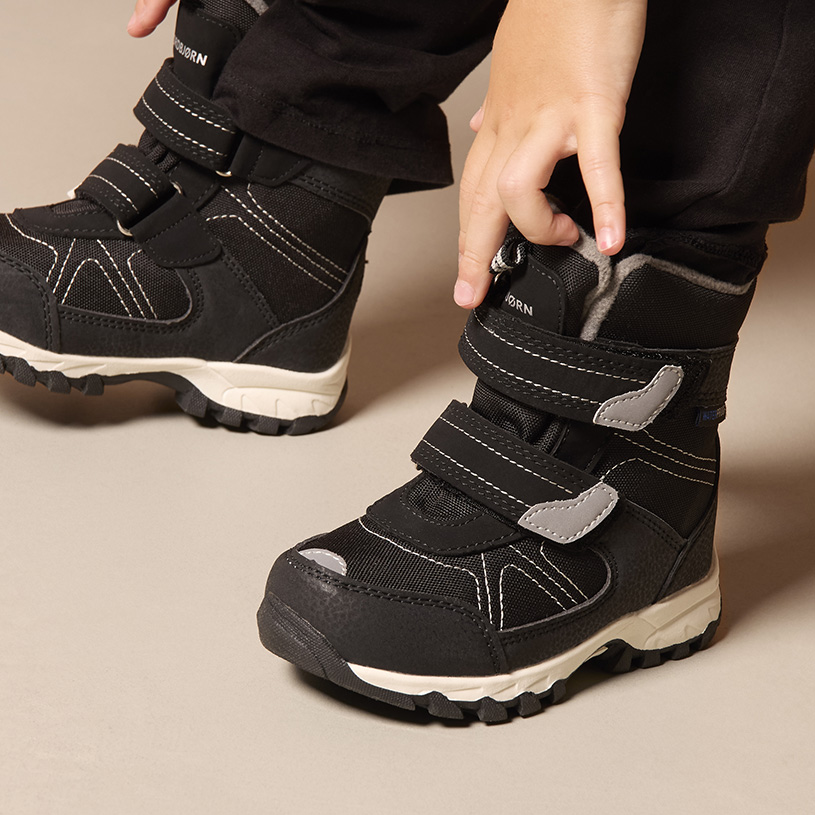 Kinderhand zieht beigen Stiefel mit Klettverschluss an.
