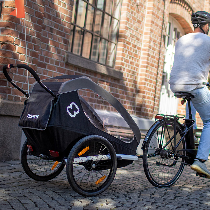 Person fährt Fahrrad mit Kinderwagen in gepflasterter Stadtumgebung.