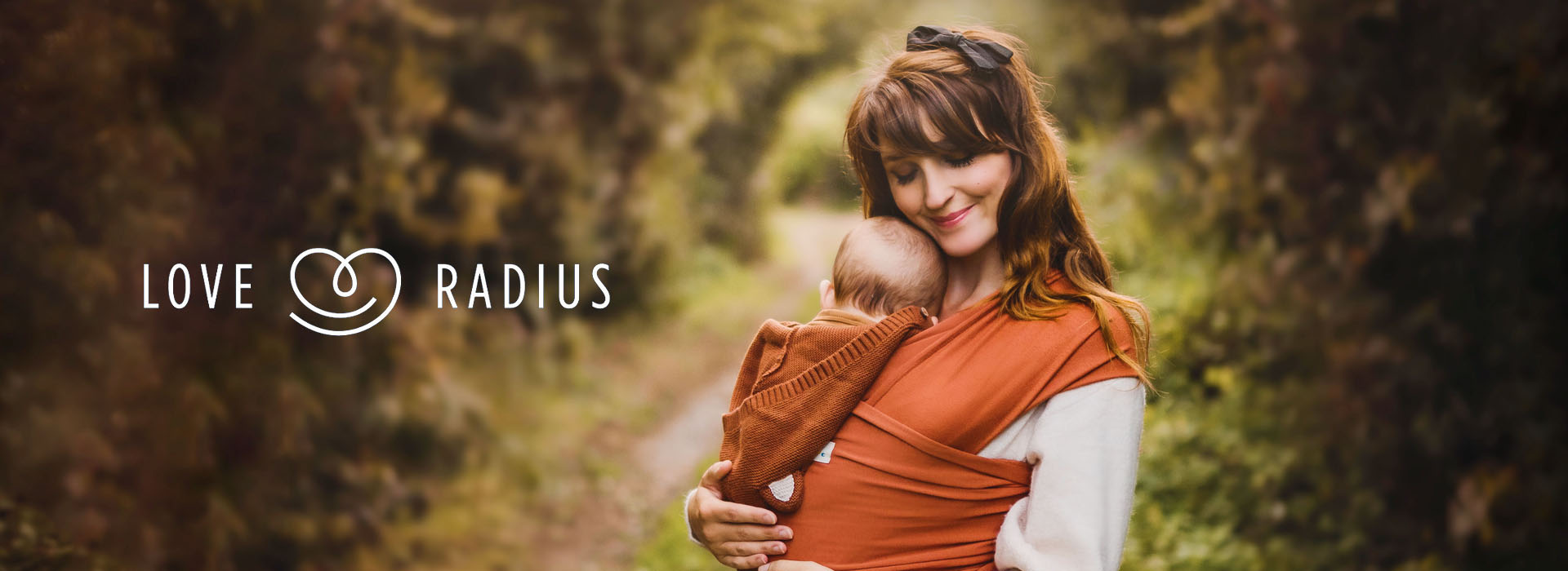 Frau hält Baby im Tuch im Waldgebiet, Logo links.