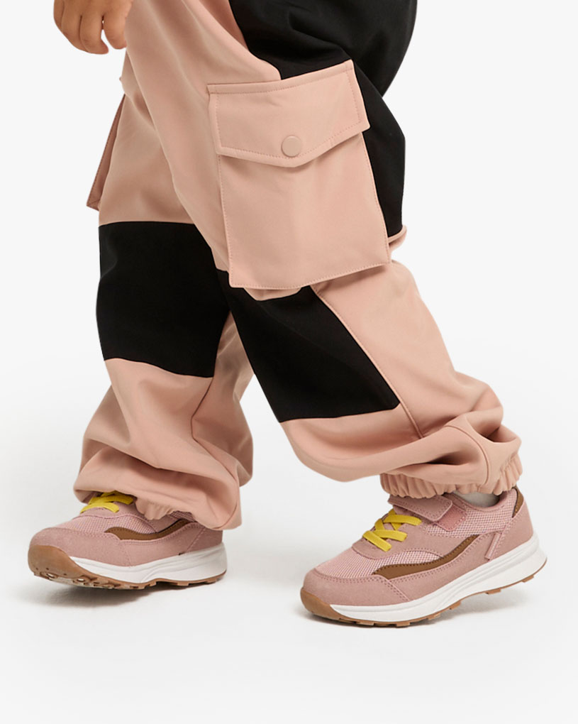 Kinderfüße in rosa Laufschuhen und grüner Hose auf Rasen.