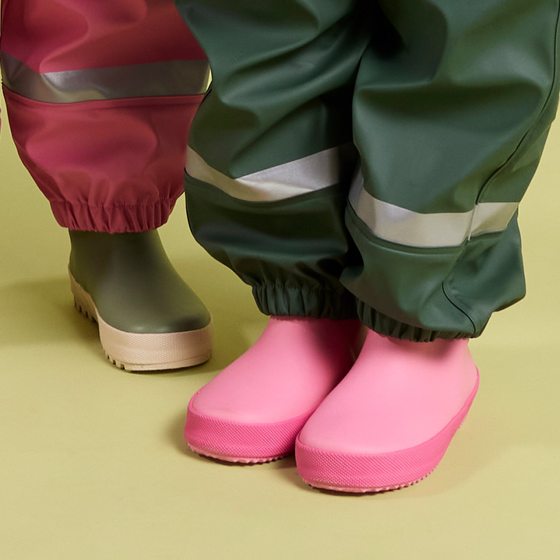 Braune Kinderstiefel mit Schmutz, auf einer Holzbank am Wasser.