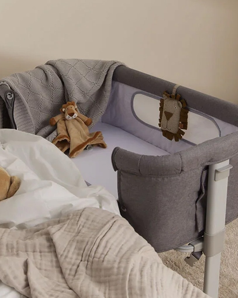 Graues Beistellbett mit Plüschtier und Decke im Kinderzimmer.