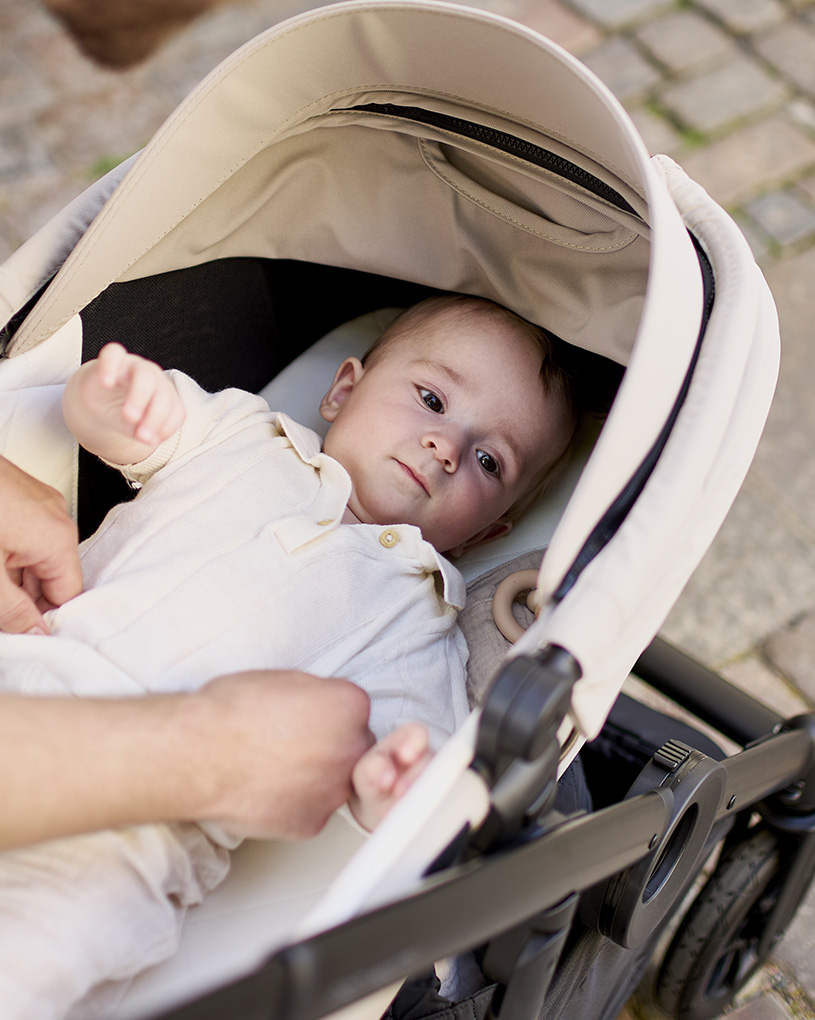 Ein schwarzer Kinderwagen mit silbernem Rahmen und braunem Griff steht auf hellem Holzboden.