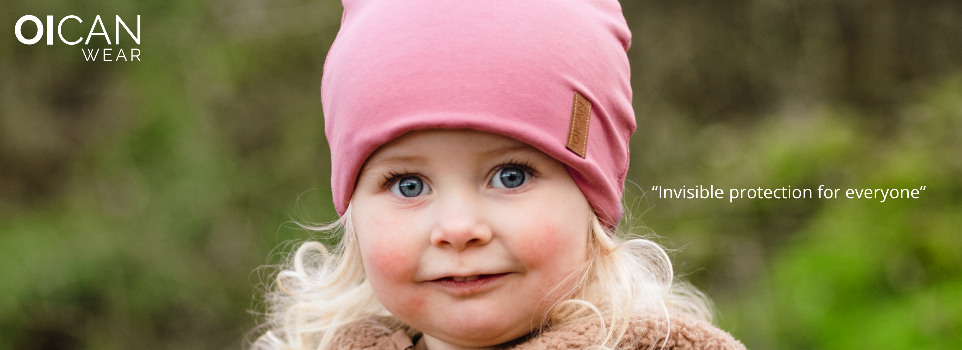 Kind in rosa Mütze vor unscharfem Naturhintergrund.