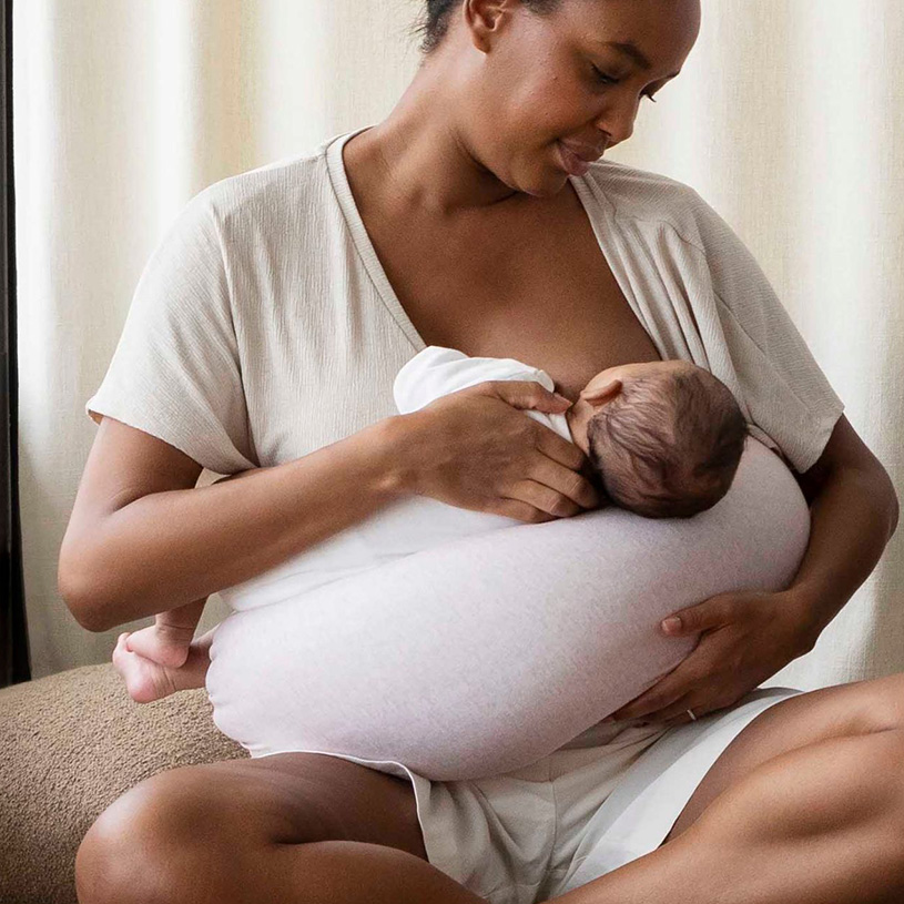 Frau stillt ihr Baby, das auf Kissen liegt.