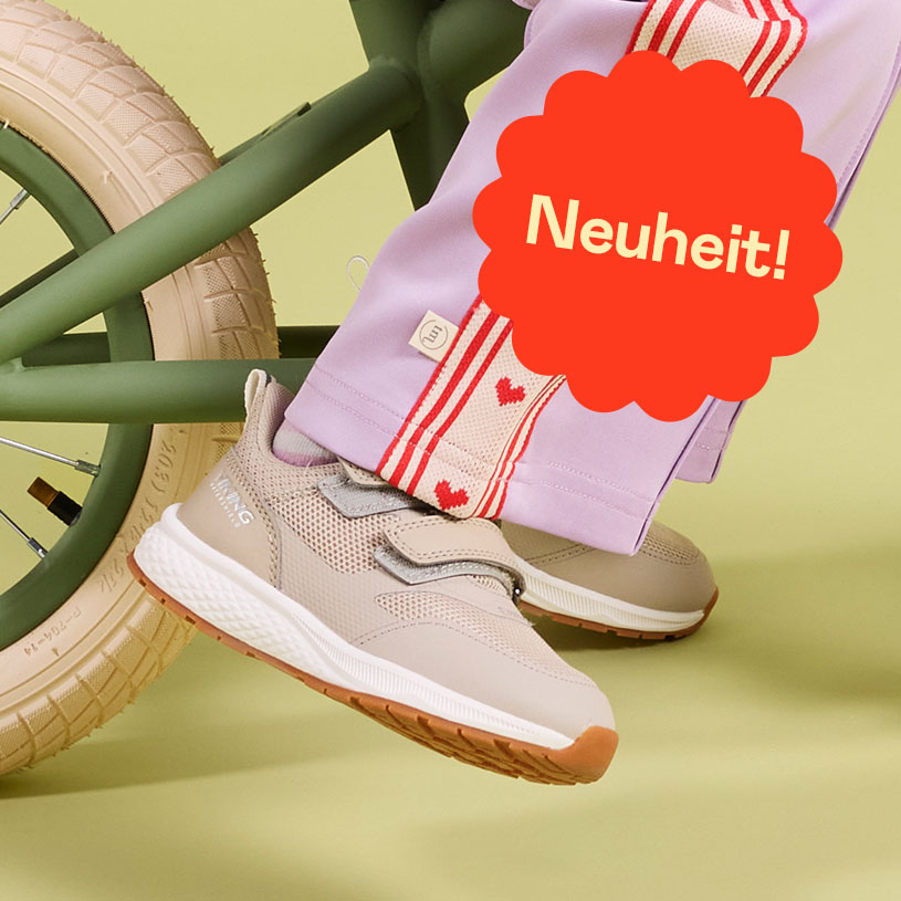 Zwei Paar Kinderfüße in verzierten Crocs im Gras mit Sprechblase: Neuheit!