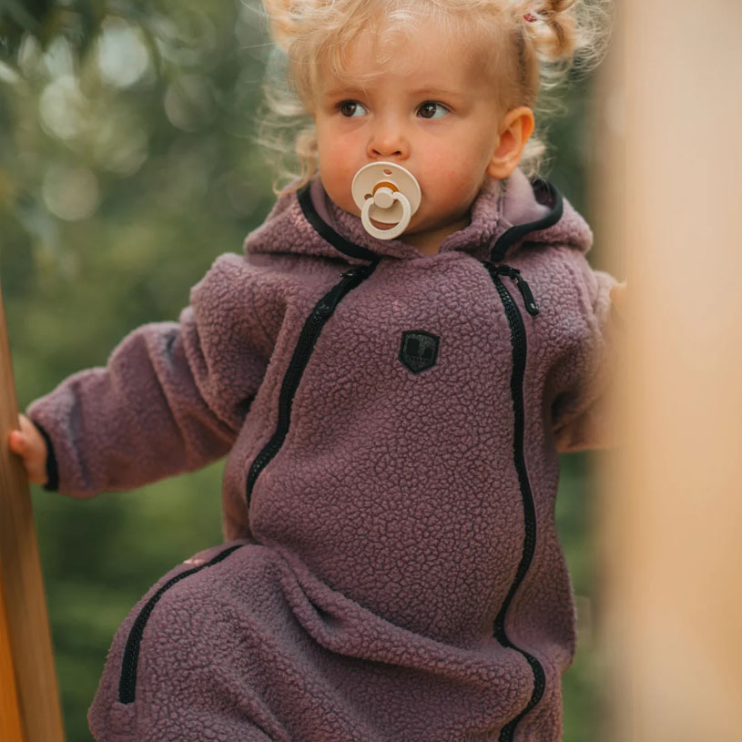 Baby in rosa Kleidung schaukelt und lächelt in einer blauen Schaukel draußen.