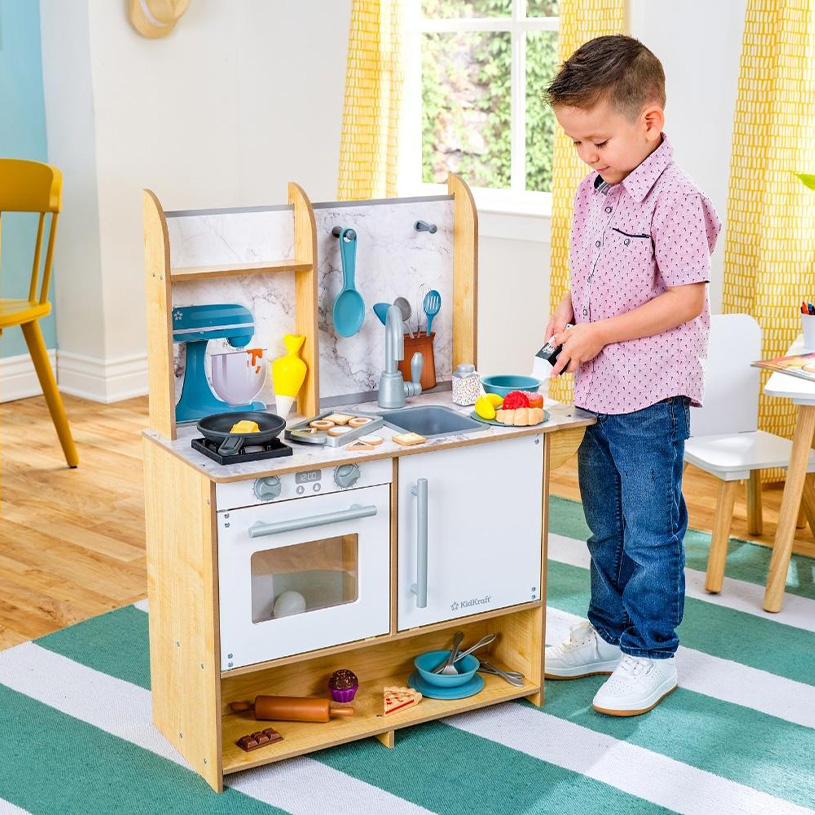 Junge spielt mit einer Spielküche und Spielzeugessen in einem bunten Raum.