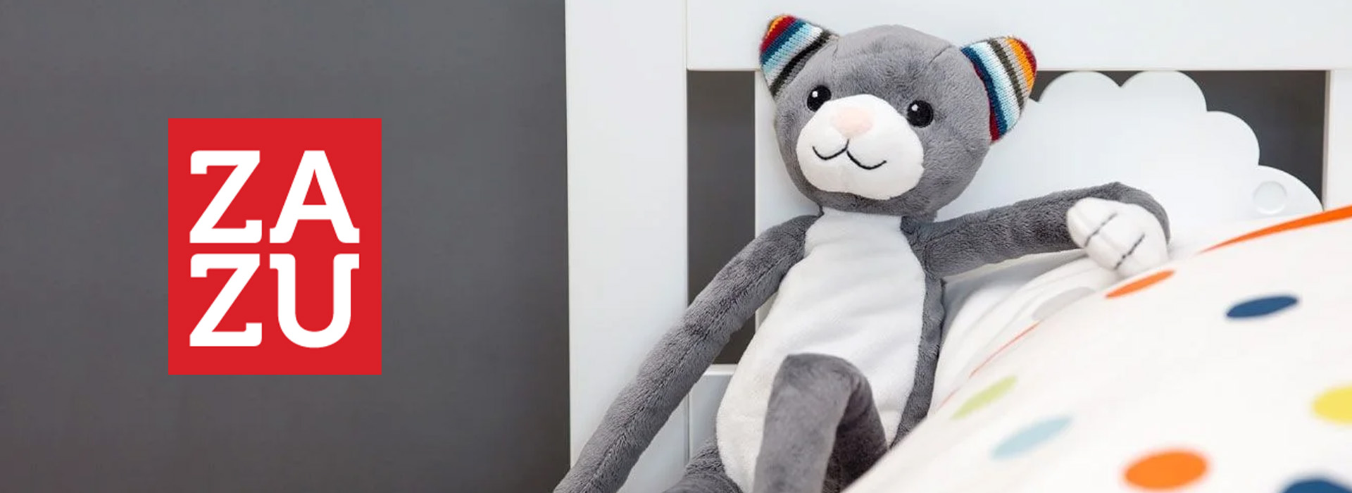 Graues Stofftier-Katze am Kinderbett neben ZAZU-Logo.