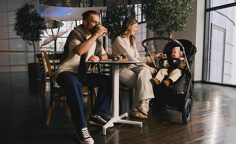 Eltern trinken Kaffee im Café mit Kind im Kinderwagen, gemütliche Stimmung.