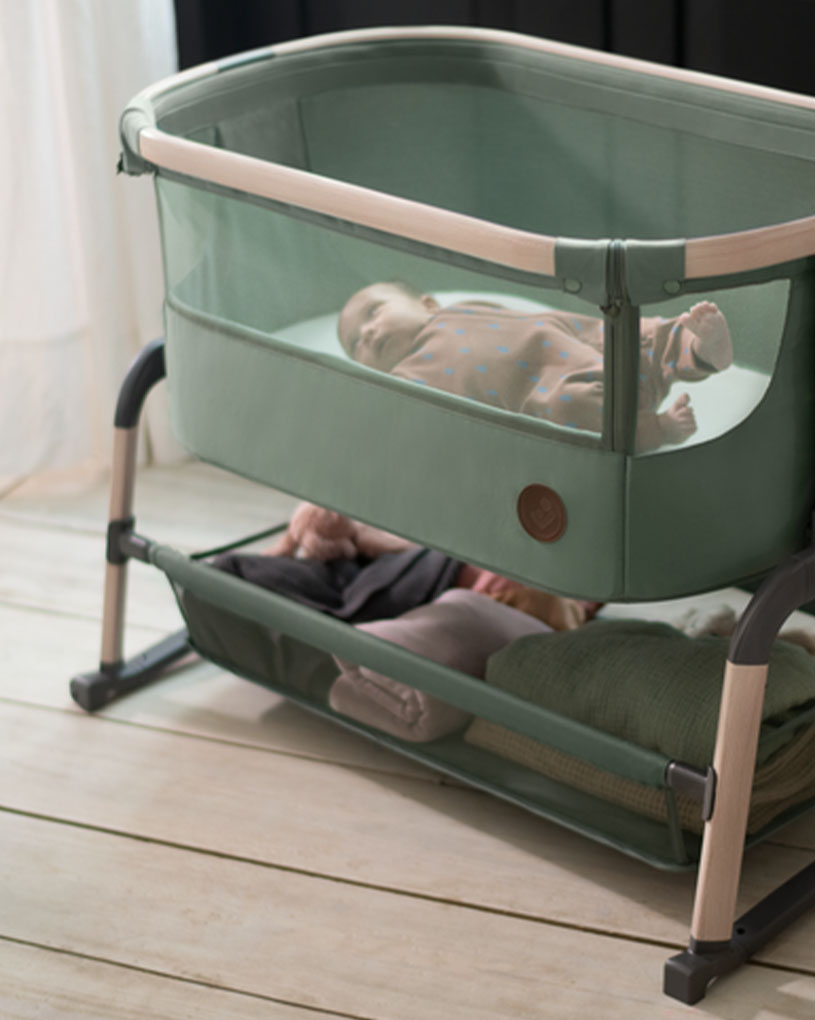 Baby schläft in grünem Kinderbett mit unterem Ablagefach.