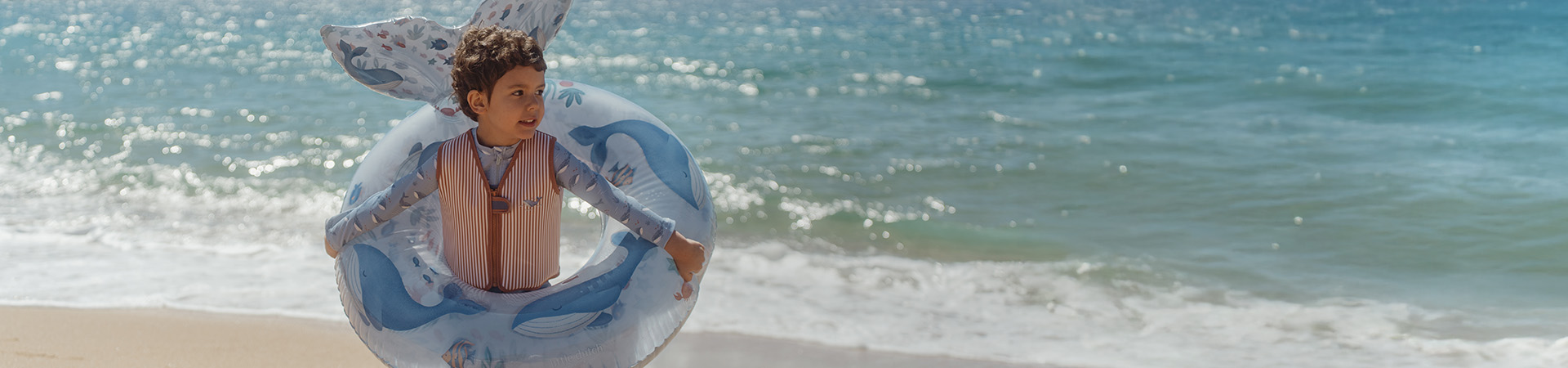 Kind am Strand mit Schwimmring, Meer im Hintergrund. Text: "Neu für die Saison".