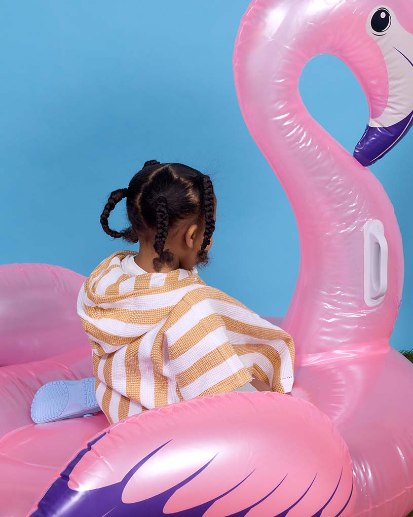 Kind in gestreifter Latzhose trägt Krabben-Schwimmreifen am Strand.