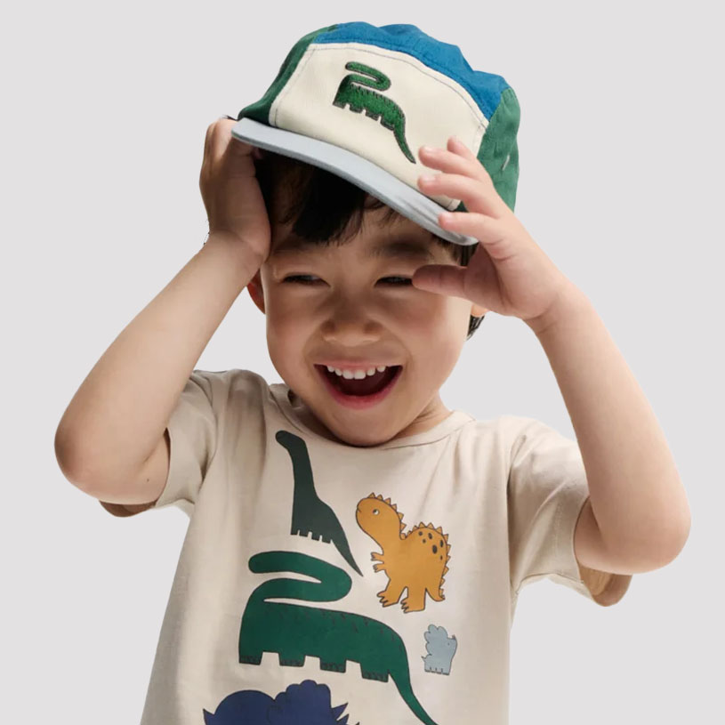 Kind mit Dinosaurier-T-Shirt und Mütze lächelt.