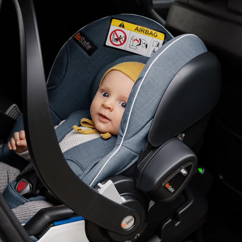 Baby im Autokindersitz mit gelber Mütze auf dem Rücksitz.