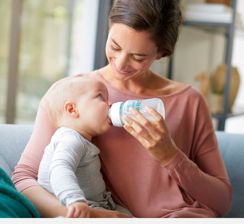 Frau füttert Baby mit Flasche auf Sofa.
