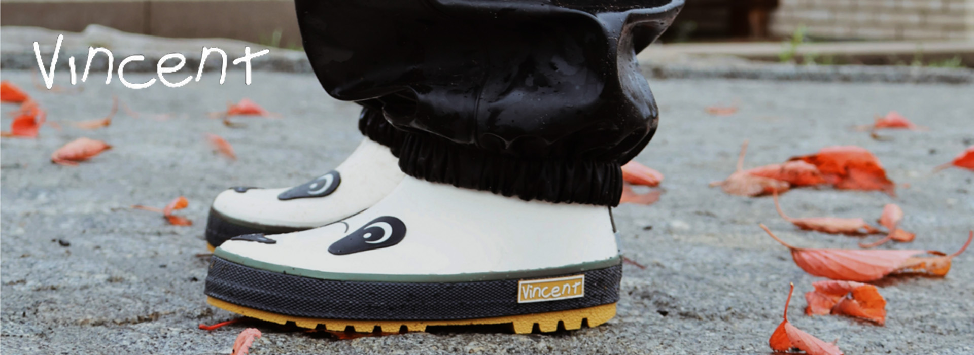 Kinderstiefel mit Tiermotiv auf einem Kiesweg mit roten Blättern.