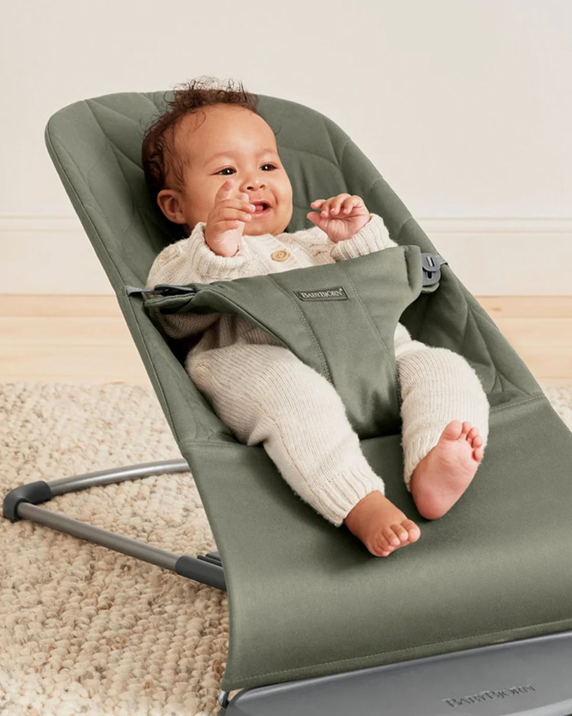 Baby in grauem Sitz, lächelt und hebt die Arme.