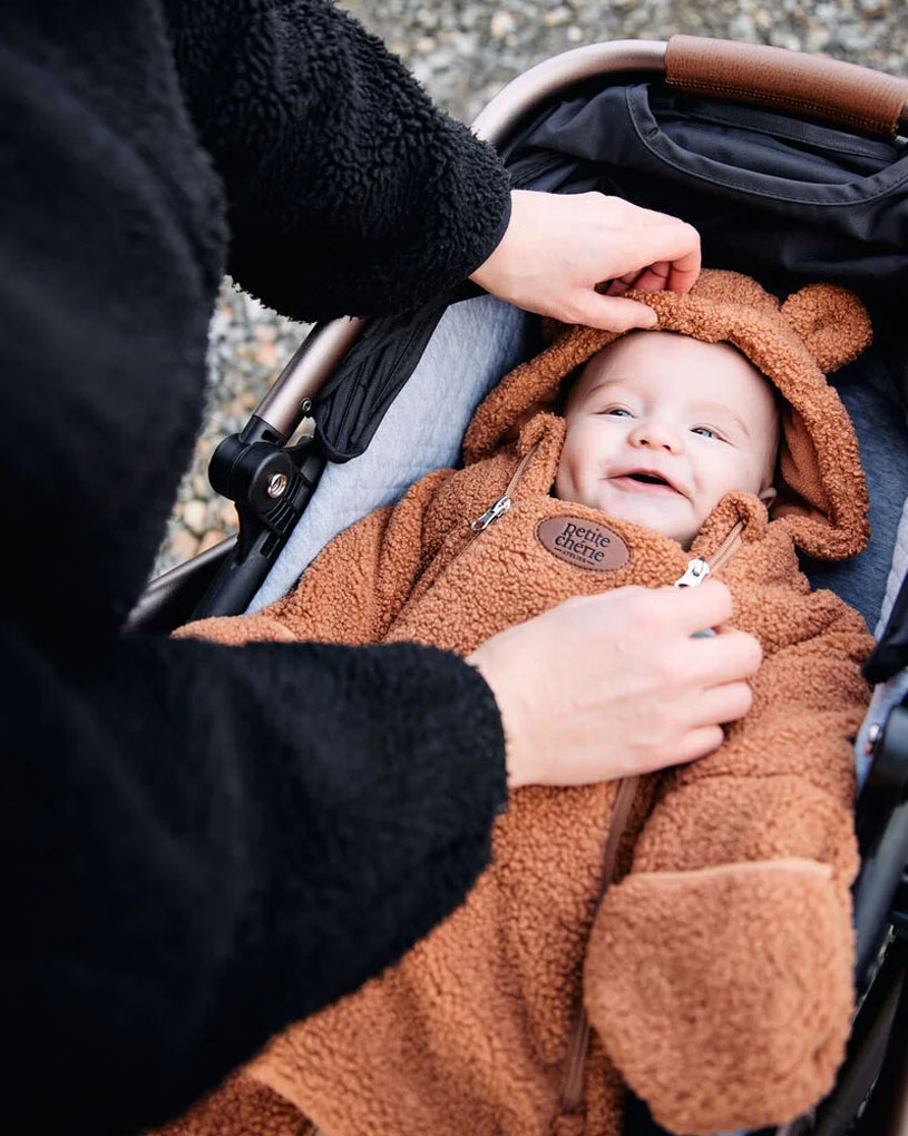 Baby im braunen Bärenanzug lächelt im Kinderwagen.