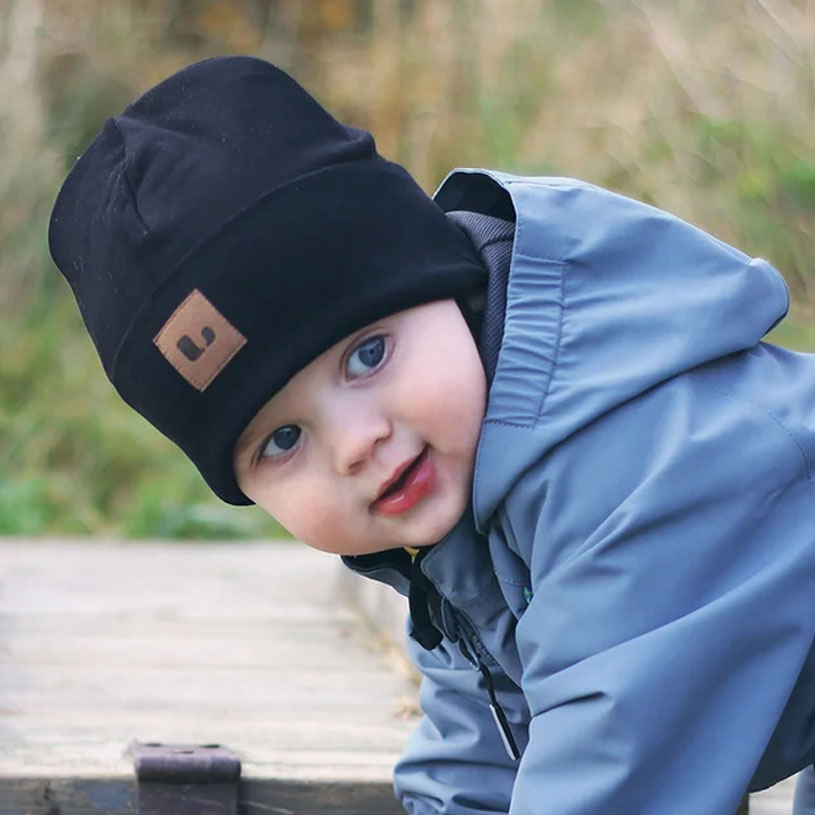 Kind in schwarzer Mütze und Jacke lächelt draußen.